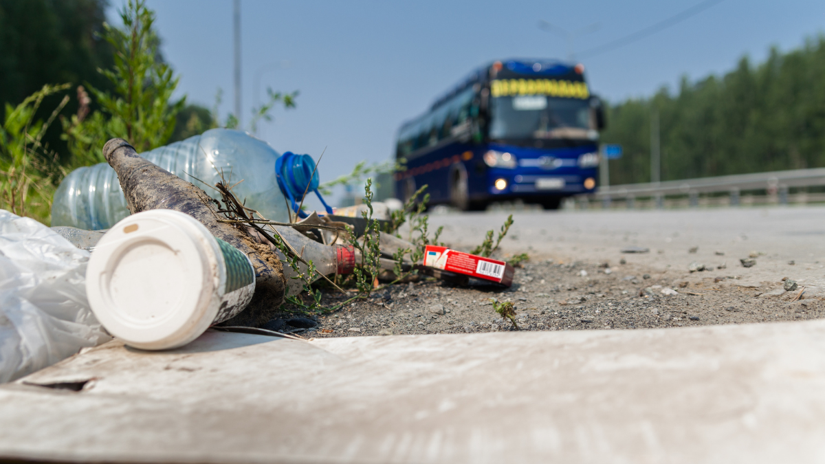 Litter is shown on the side of a road as a blue bus approaches.