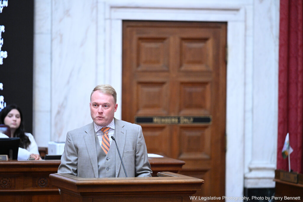 A man wearing a grey suit speaks from a podium in the West Virginia House of Delegates.