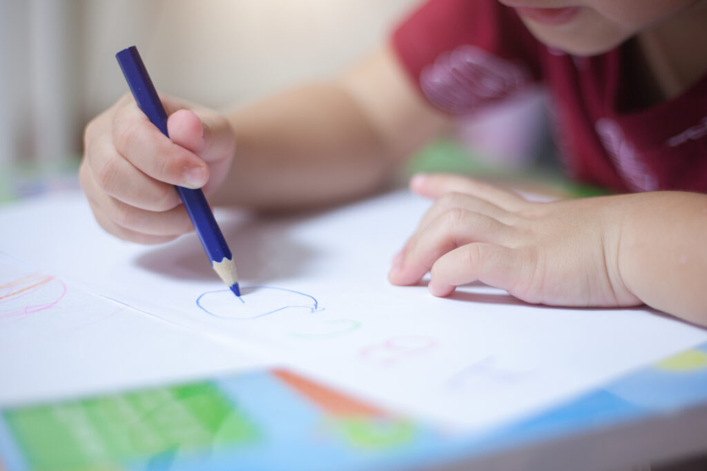 A child's hands are seen drawing with a blue pencil.