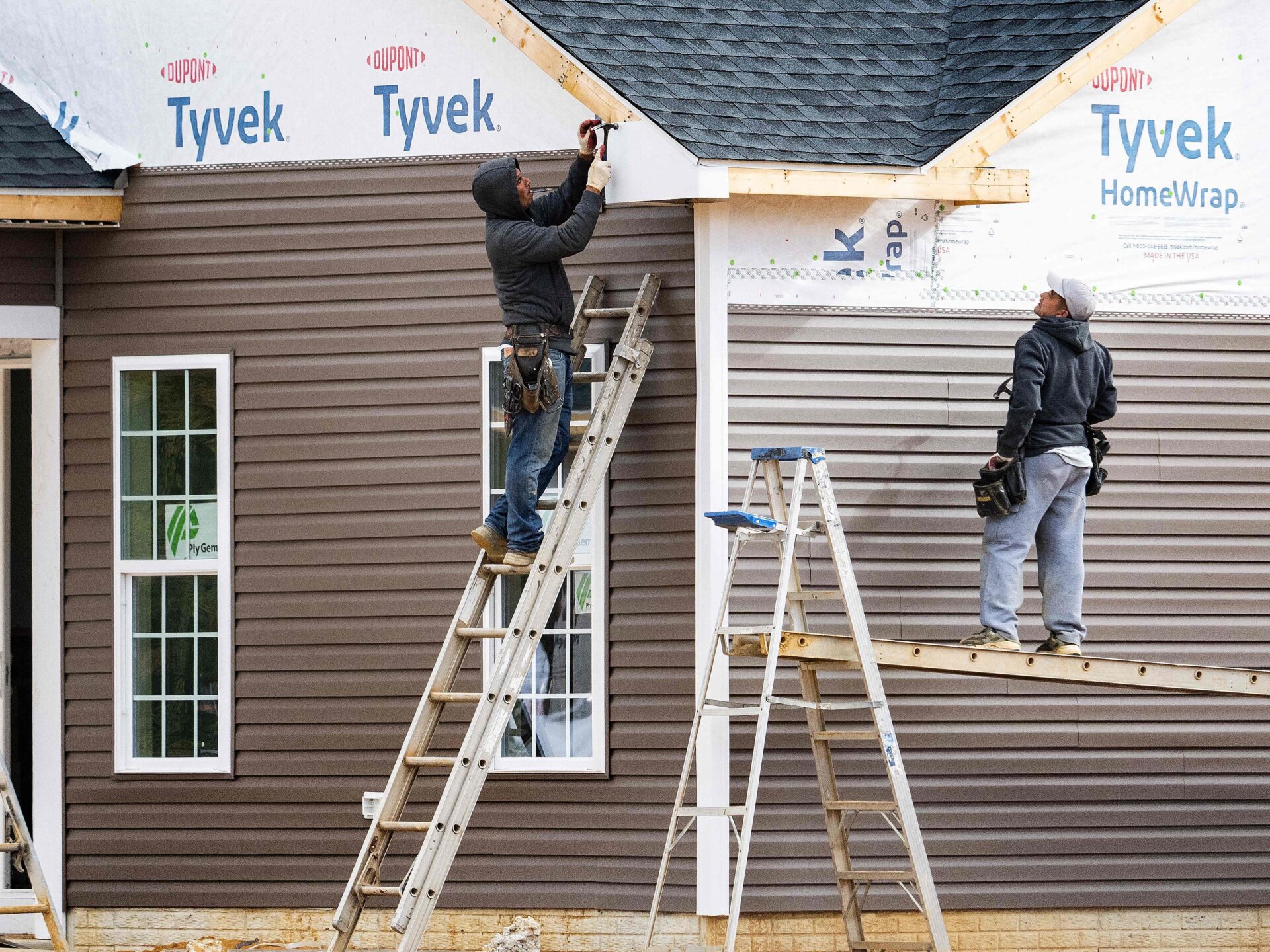 Workers on ladders putting siding on a house.