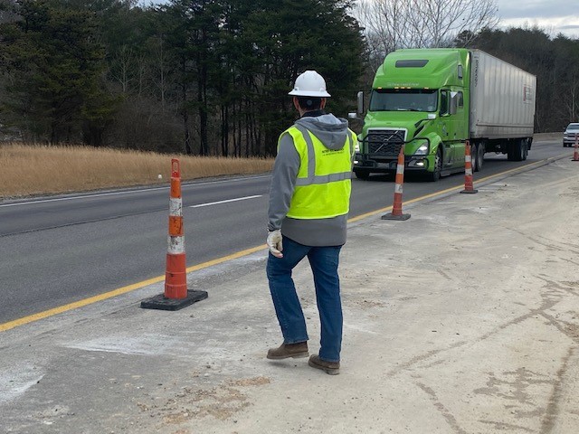 Man in reflective vest next to interstate lane lined with safety cones