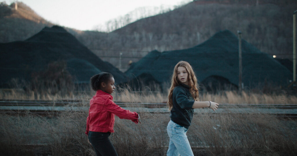 Two children walk down a road. Mountains are seen in the distance.