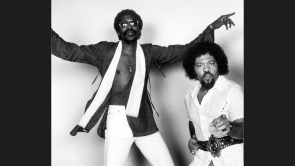 Two Black men from the 1980s in stage clothes.