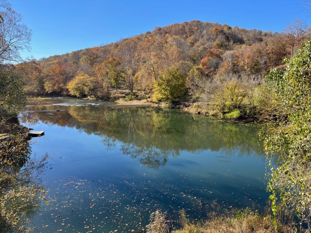 Calm water reflects the fall foliage and clear sky in a scene along the Elk River.