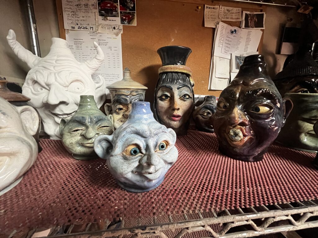 Several face jugs, all different colors and sizes, are seen on a shelf.