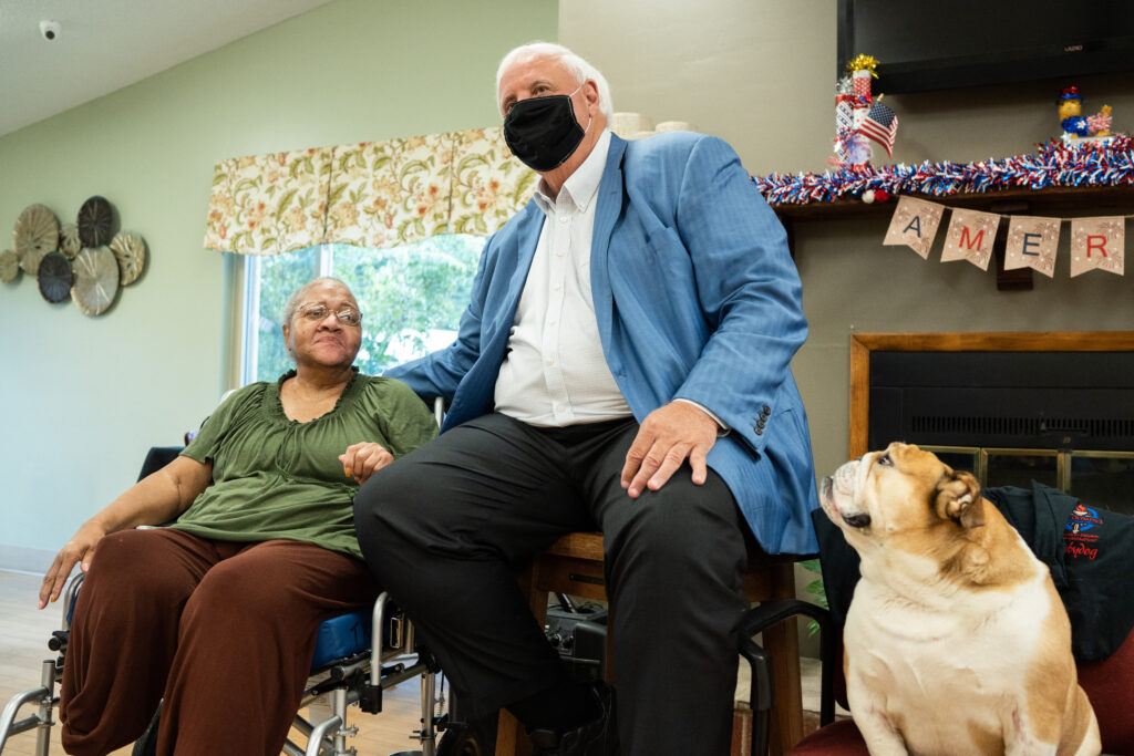 Big man in mask visiting with nursing home resident.