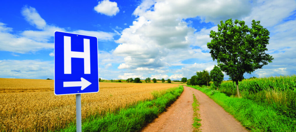 A blue sign pointing toward a hospital is seen on a rural road.