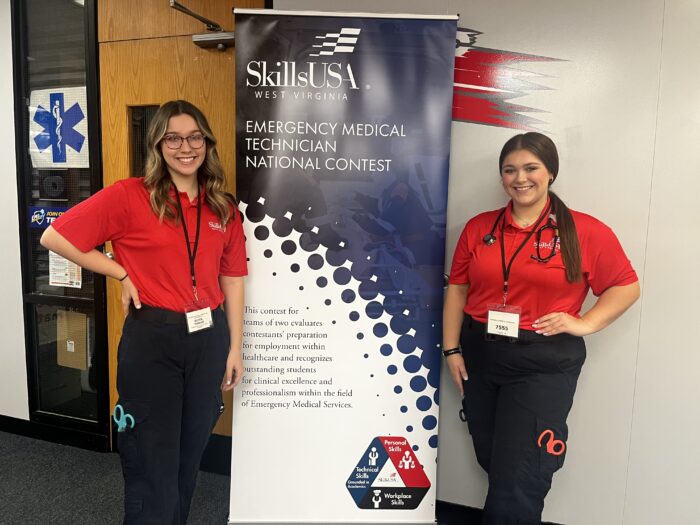 Two young women in EMT garb standing near a banner.