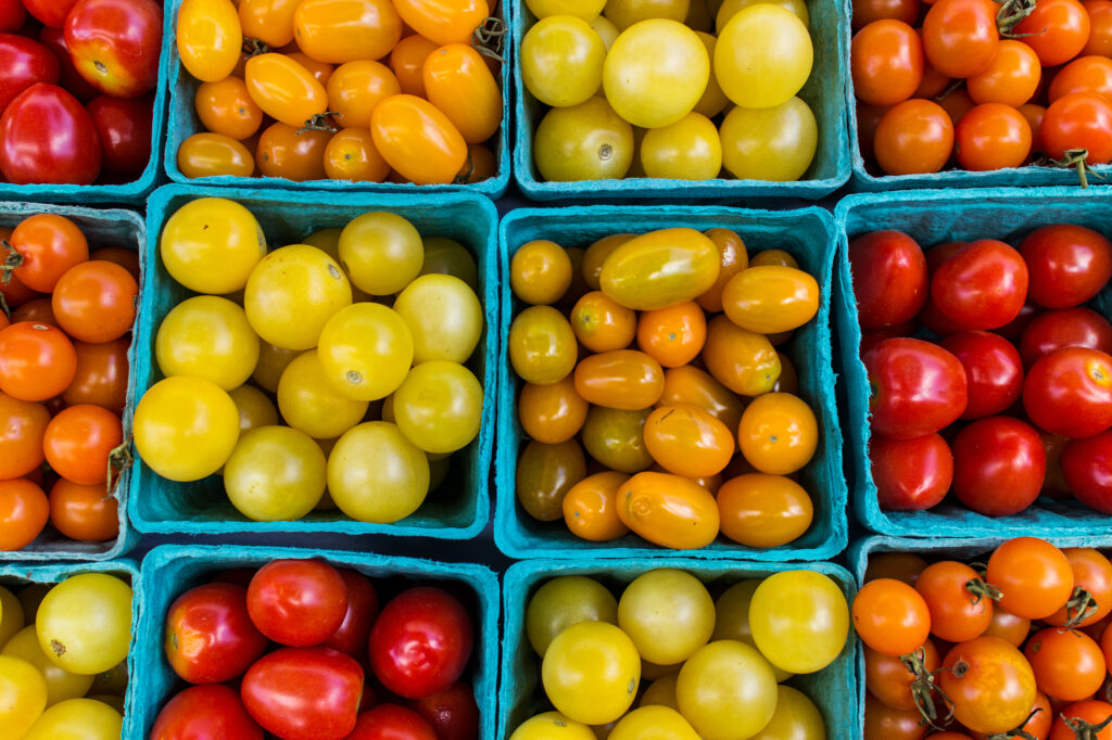 Different colors and types of tomatoes are displayed at a farmer's market.
