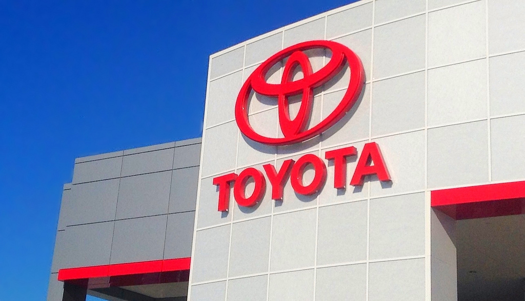 The red Toyota logo, along with the word Toyota, is displayed on a white-paneled building with red accents.