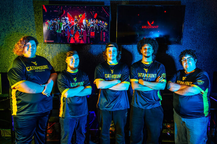 Five people stand in teh line with their arms crossed, bathed in yellow and blue light