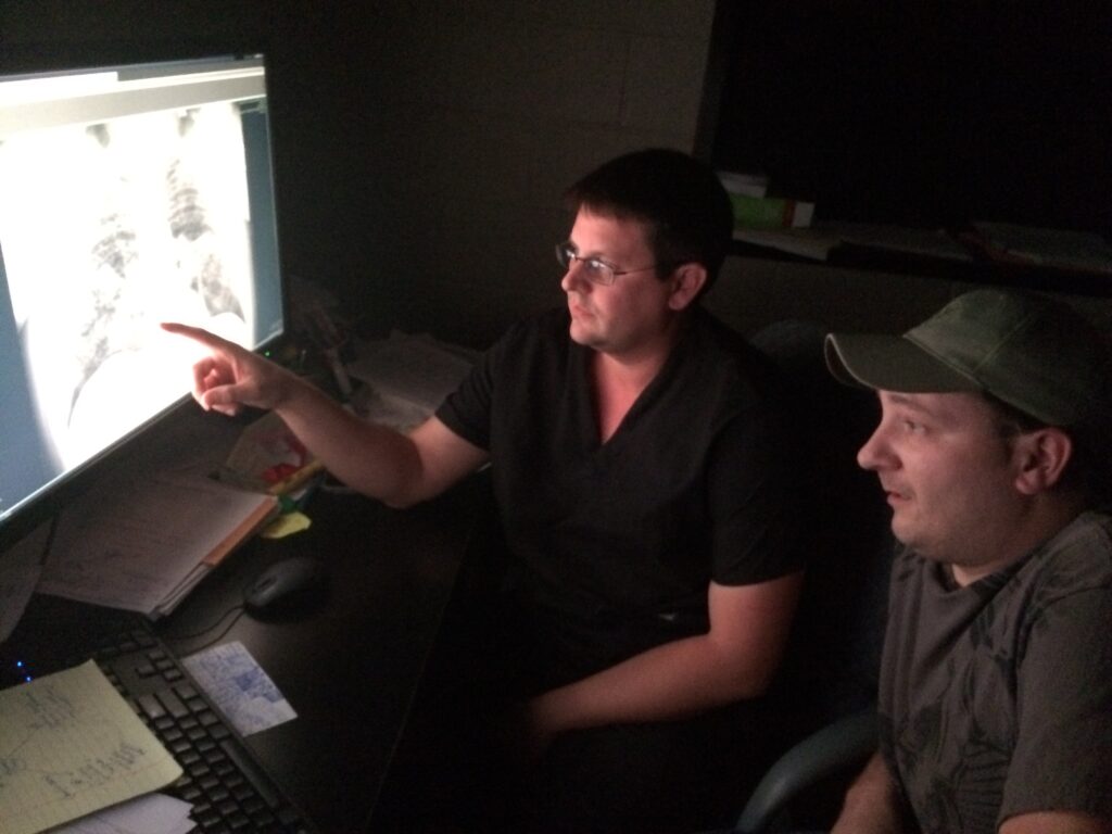 Two men are seated in front of a computer screen displaying an x-ray of black lung disease.