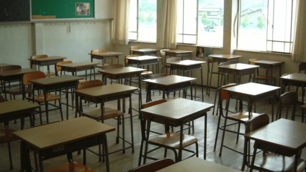 A vacant classroom with rows of wooden desks and chairs.