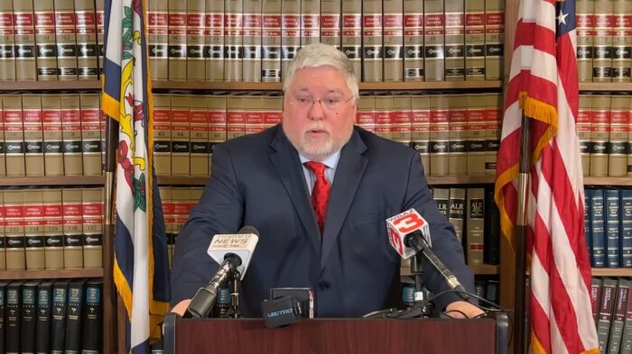 Gray-hair man in a suit with a red tie stands behind a podium.