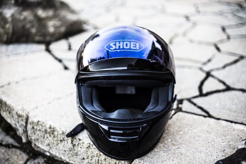 A blue wraparound motorcycle helmet with the brand name "Shoei" on the forehead sits on a paved step.