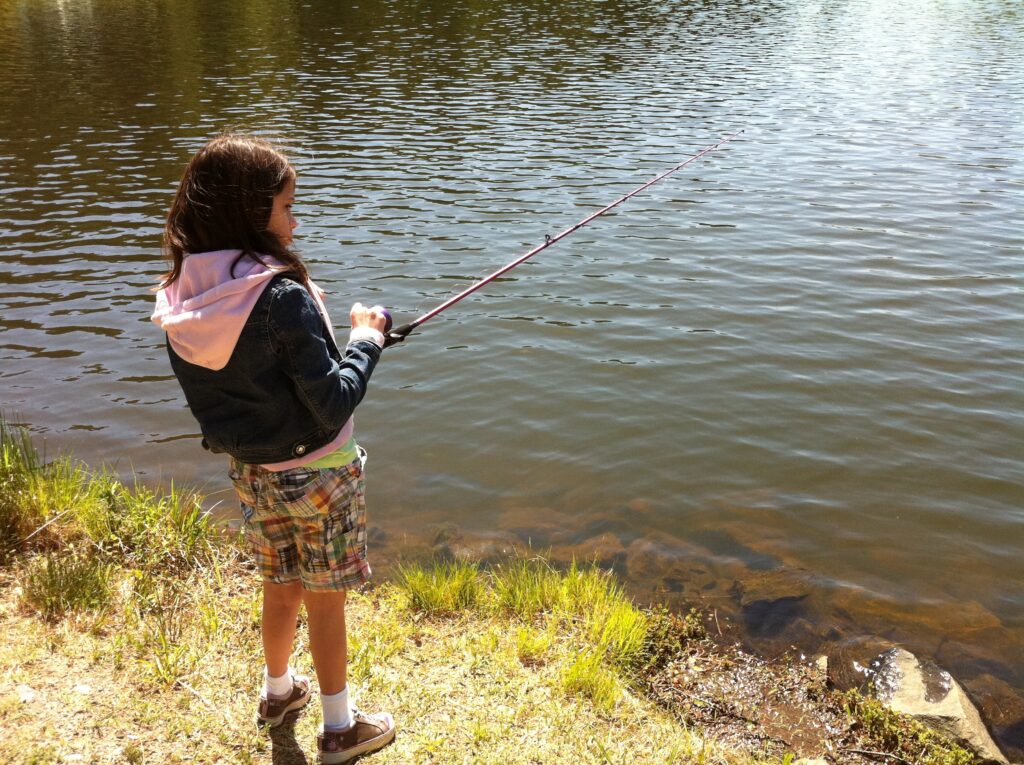 Young girl in shorts holding fishing rod over water.