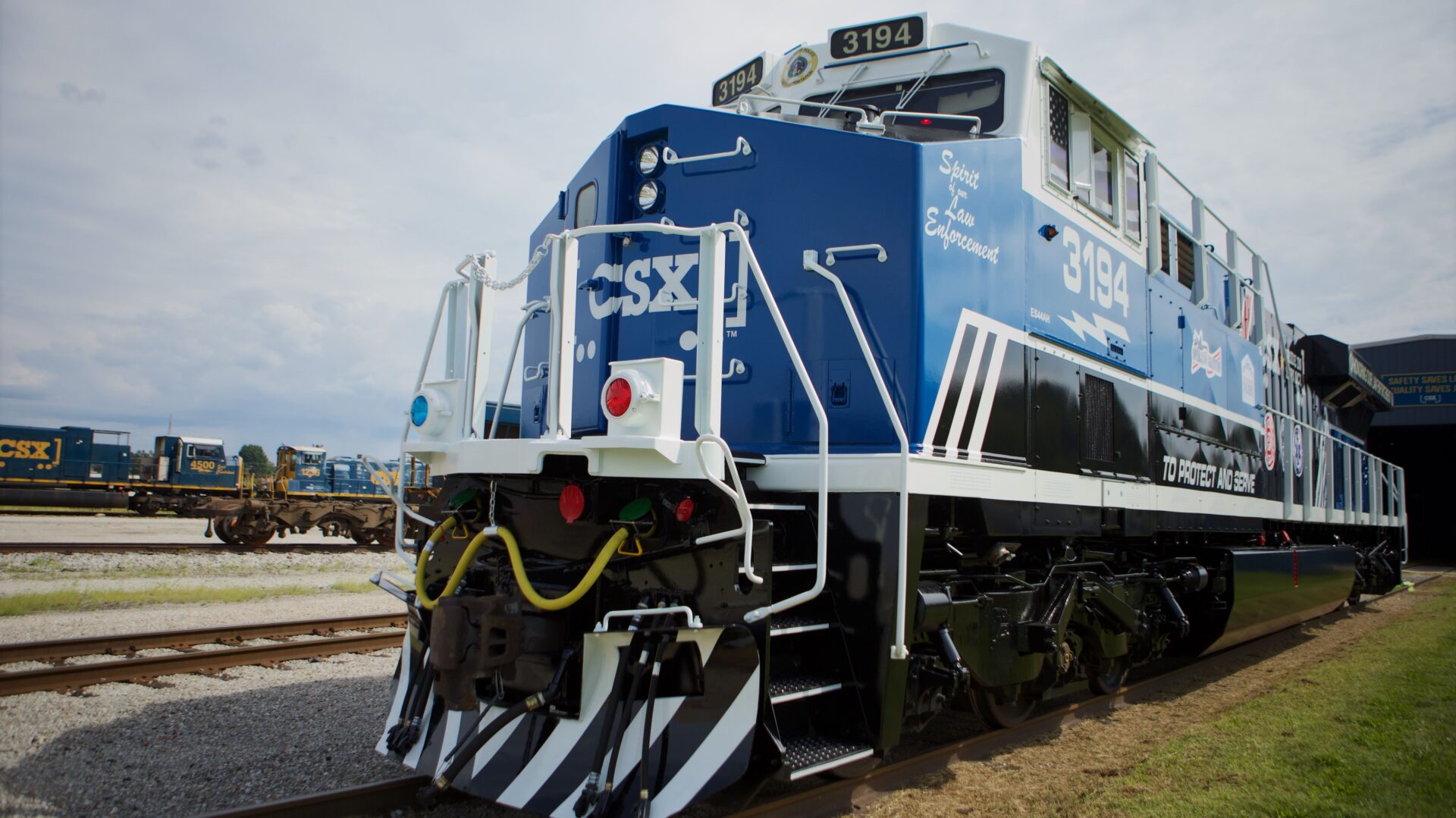 A blue and white CSX locomotive is painted to honor law enforcement. It sits prominently with other locomotives in the background.