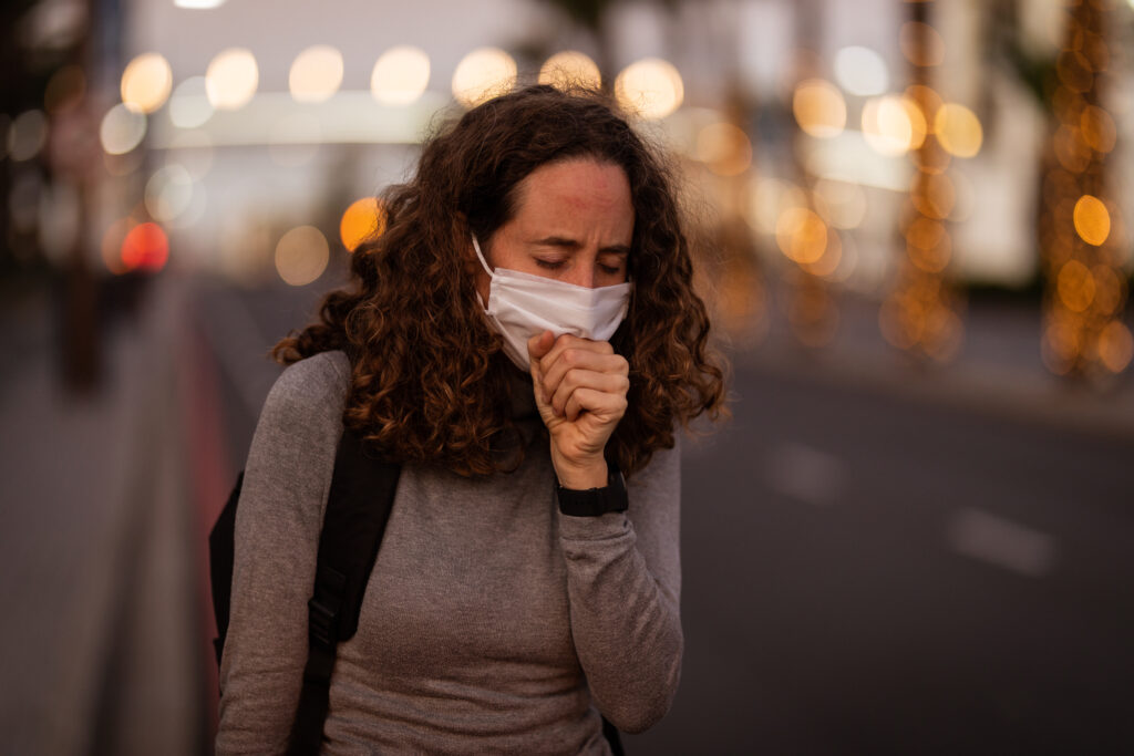 Caucasian woman wearing a protective mask and coughing in a city street.