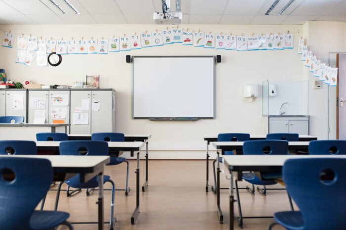 School desk and chairs in empty modern classroom. Empty class room with white board and projector in elementary school. Primary classroom with smart board and alphabet on wall.