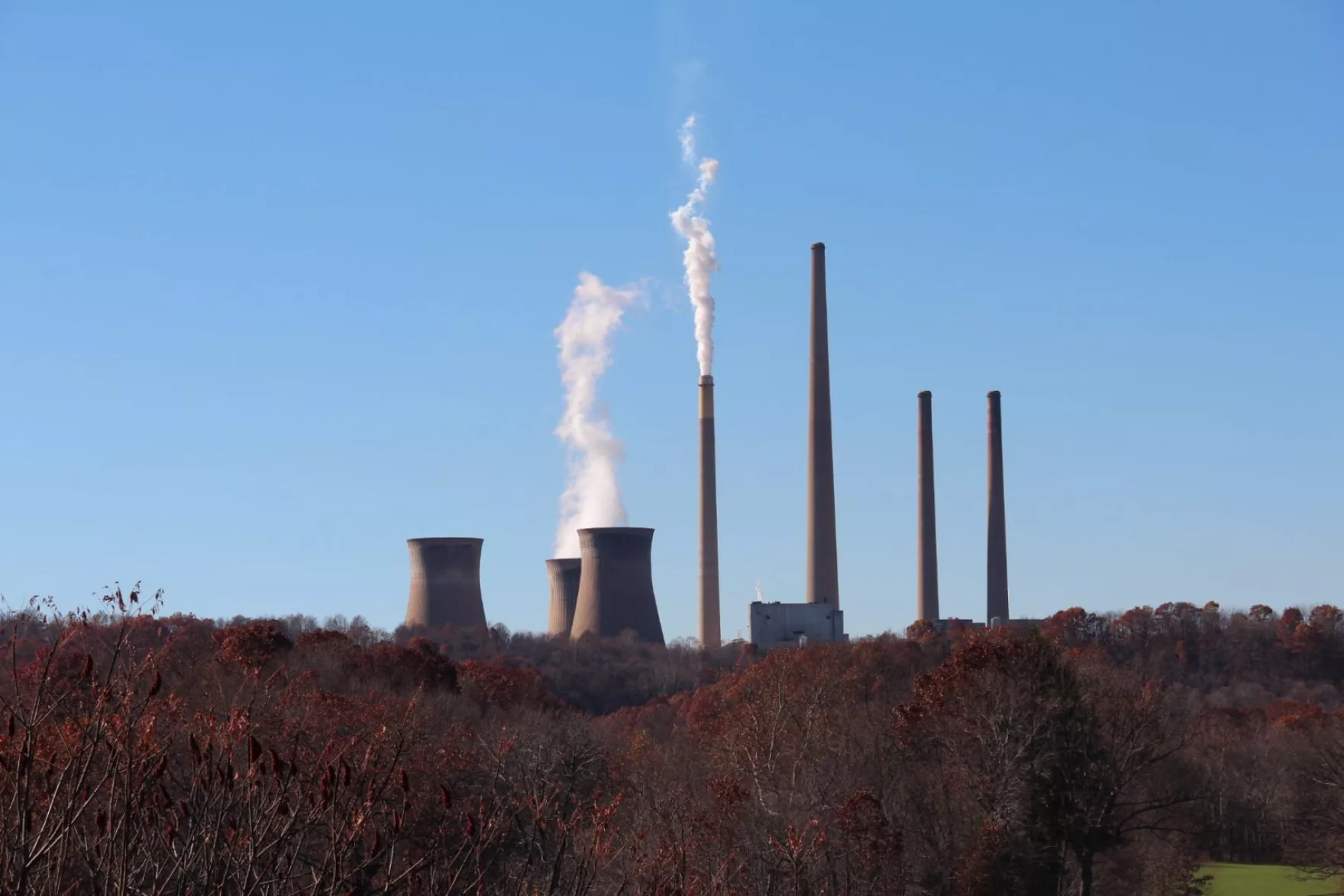 A power plant, with cooling towers and smokestacks, is visible from a distance on a clear winter day.