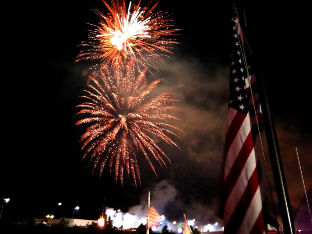 A bright display of fireworks lighting up the sky behind the American flag.
