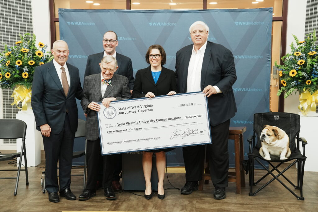 A group of people in suits pose alongside a large check being awarded.