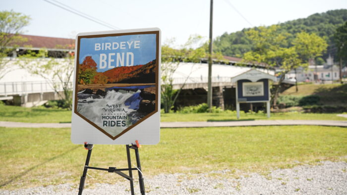 Sign showing new mountain driving trail name in front of covered bridge.