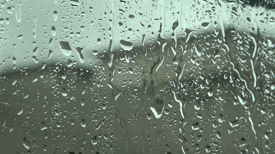 Water on a pane of glass runs down in the foreground of a grey, undefined scene.