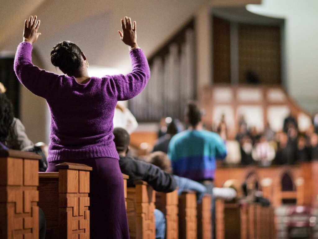 A woman is seen from behind raising her hands in worship during a church service.