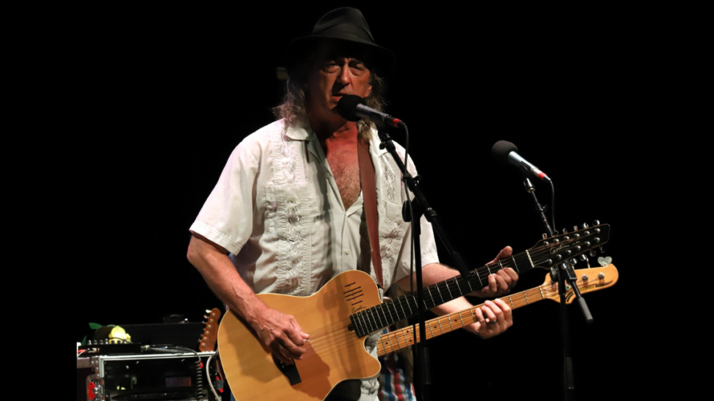 A man with long hair and a hat plays the guitar.