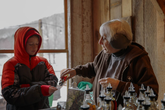 An older woman gives a young boy maple syrup.