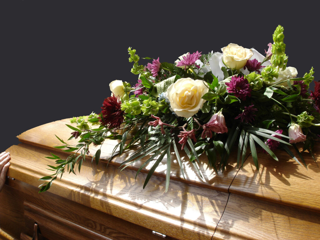A closed brown, wooden casket with colorful flowers laying on top.