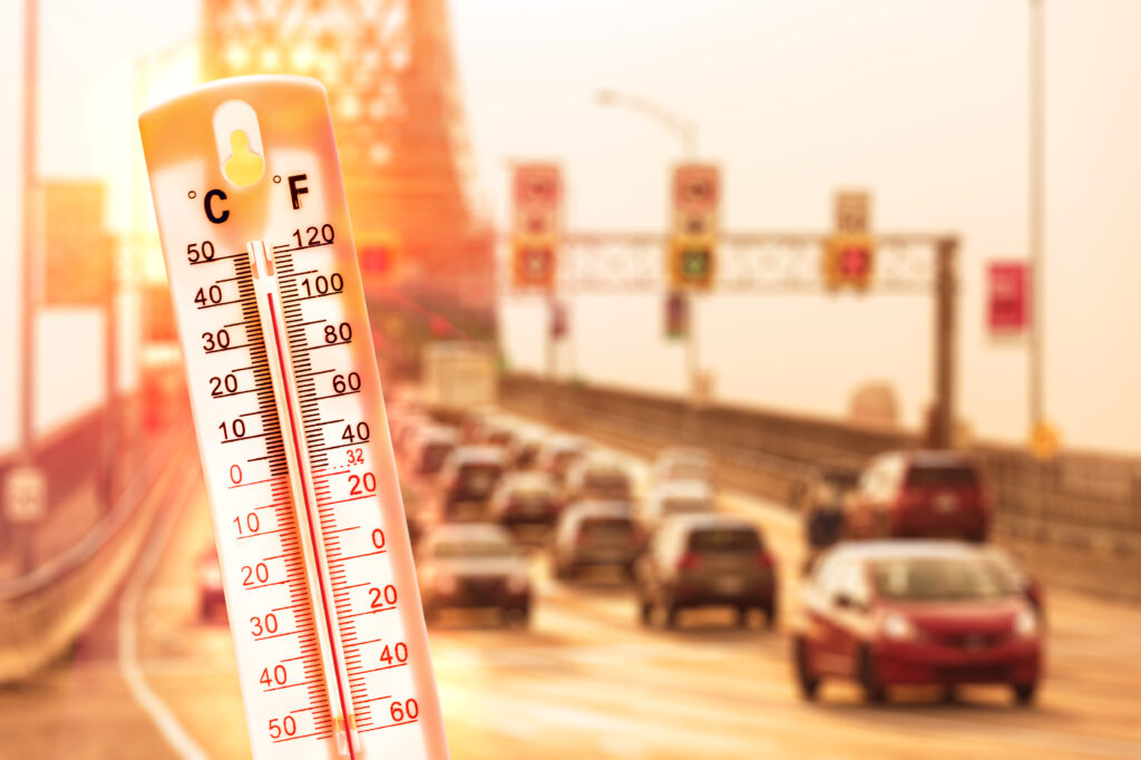 Thermometer in front of cars and traffic during heatwave.