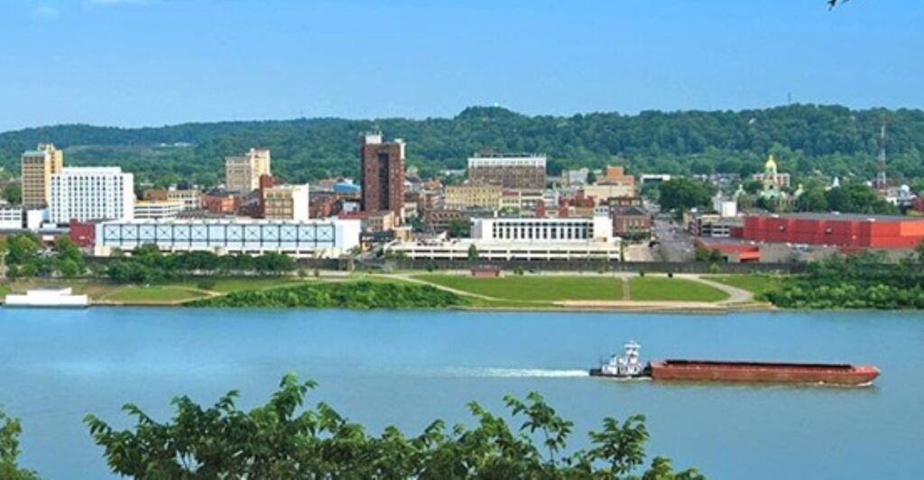A coal barge makes its way up the Ohio River and passes in front of the city of Huntington skyline.