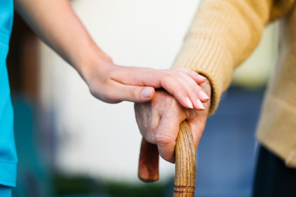 Doctor holding a senior patient's hand on a walking stick.