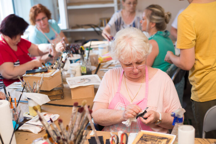 An older woman sits at a craft table.