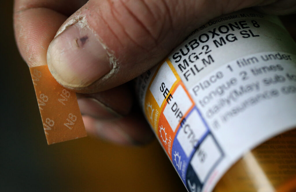 A prescription pill bottle and a dissolvable strip are seen in someone's hand.