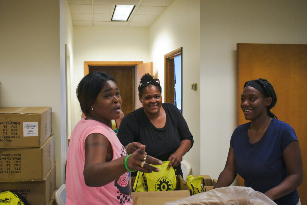Three women are seen smiling while packaging health kits