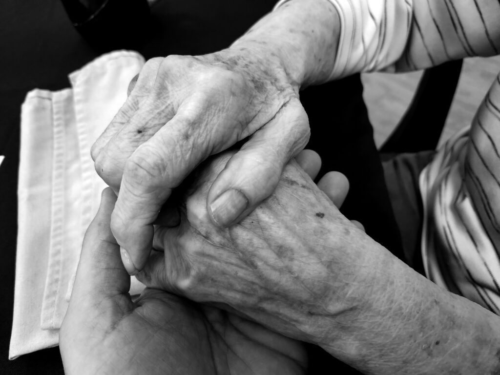 Black and white photograph of a close up of elderly hands being held by younger hands.
