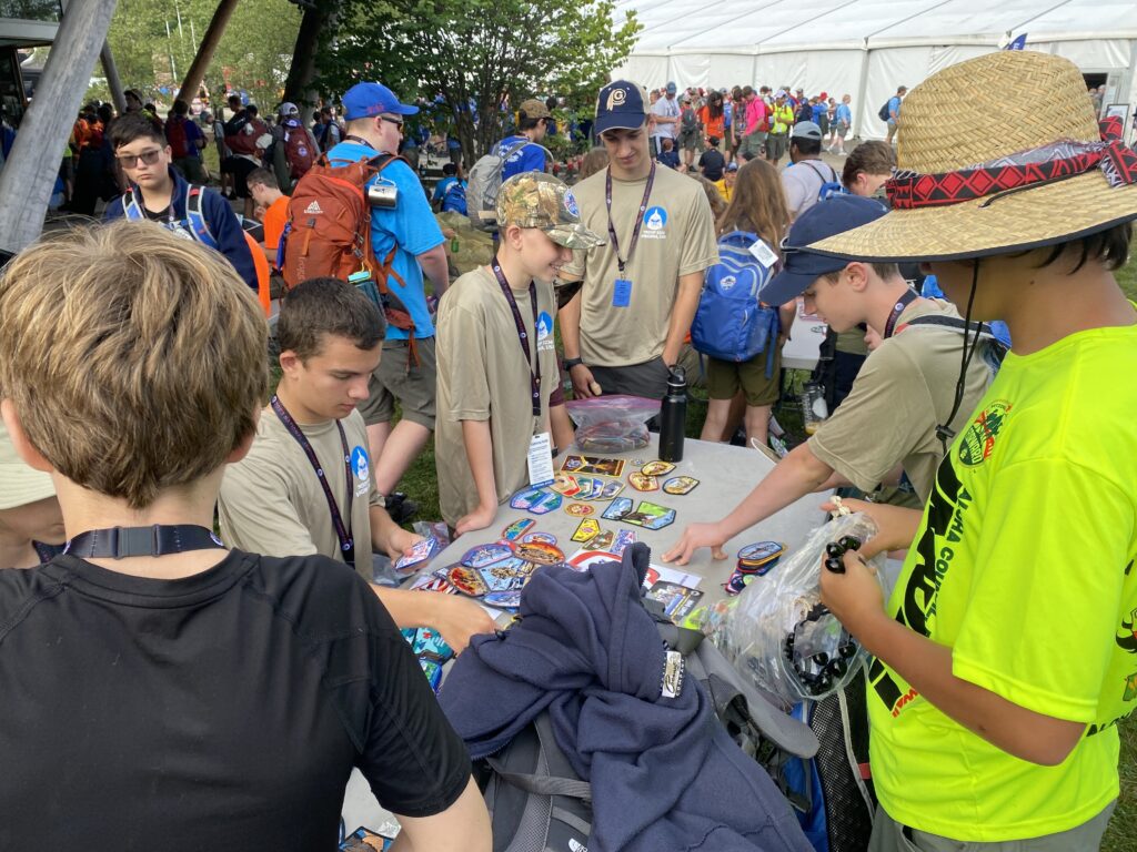 More than six teenage boys are seen dressed in their scout gear. They are seen wearing lanyards and hats and trading scout patches.