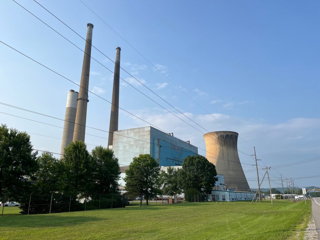 An idled power plant sits in silence on a hazy summer day as seen from the side of a state highway with empty stacks soaring into the sky.