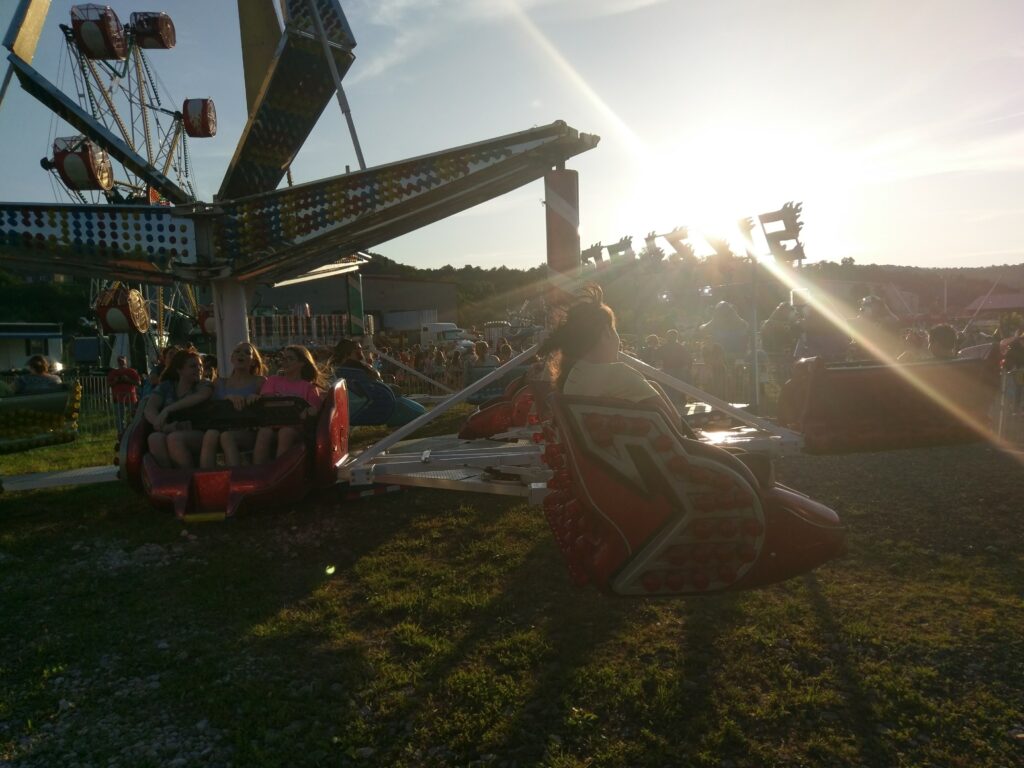 Young people riding an amusement park ride with the sun setting in the background.