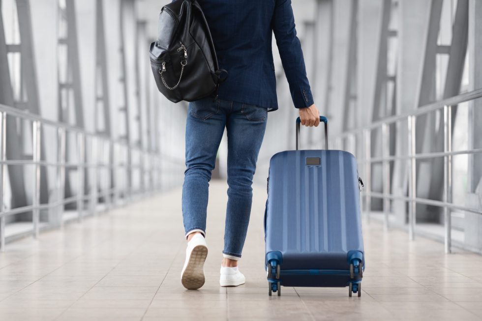 A woman wearing blue jeans and a blue top walking through an airport pulling a carry on bag.