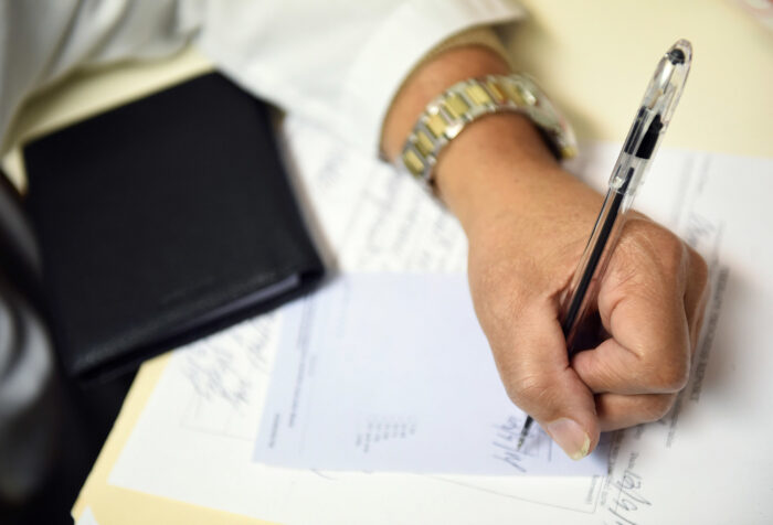 A doctor writes a note on paperwork with a black pen.