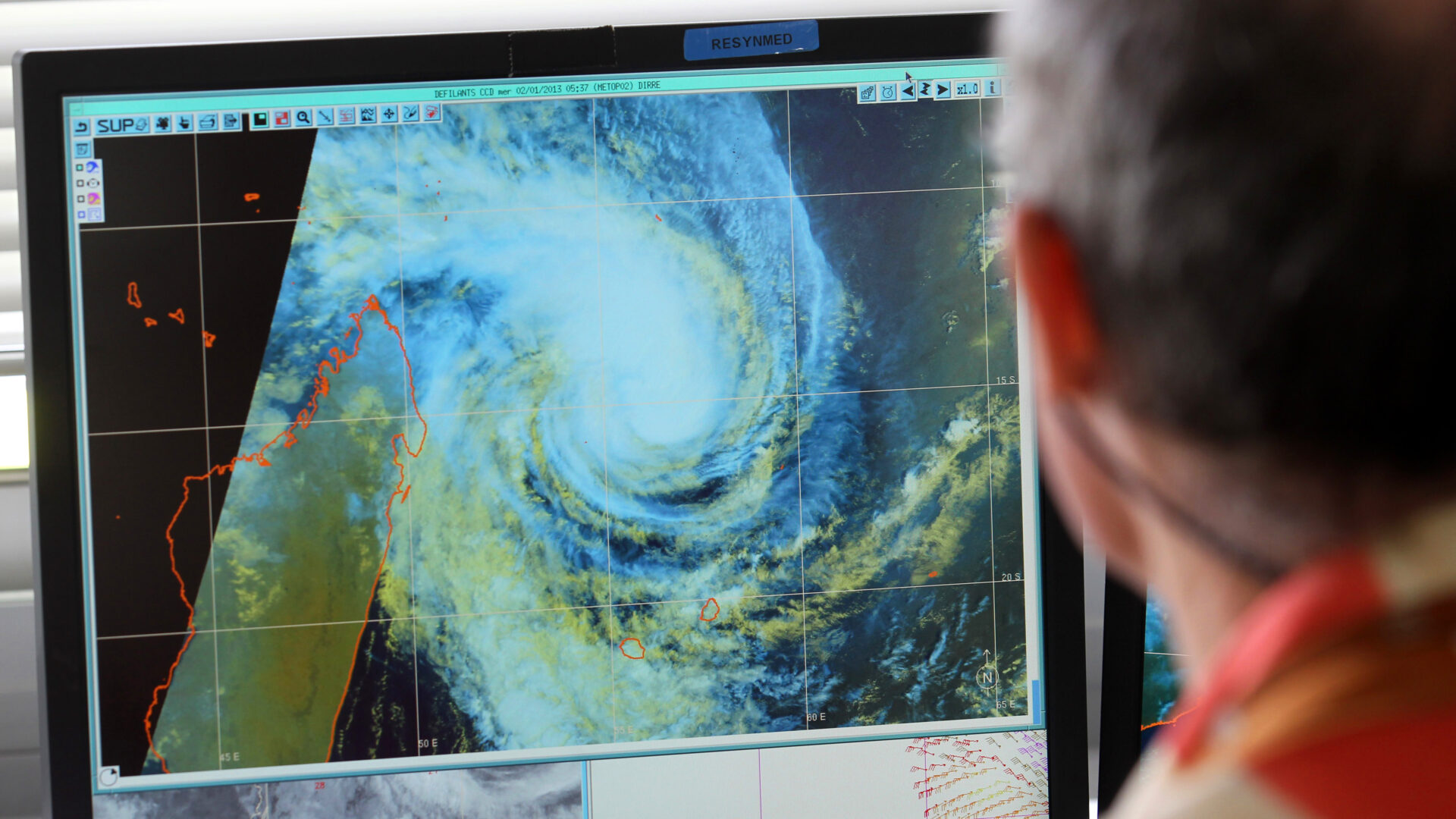 A man looks at a digitized rendering of a cyclone on a computer screen.