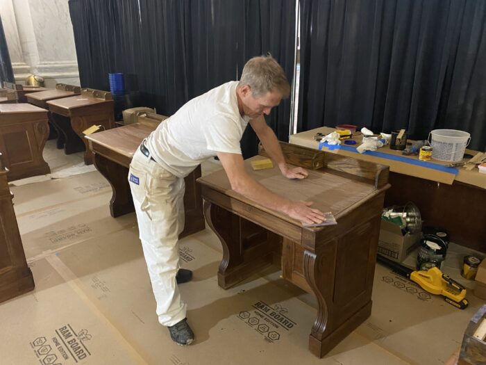 A man finishes large wooden desks. 