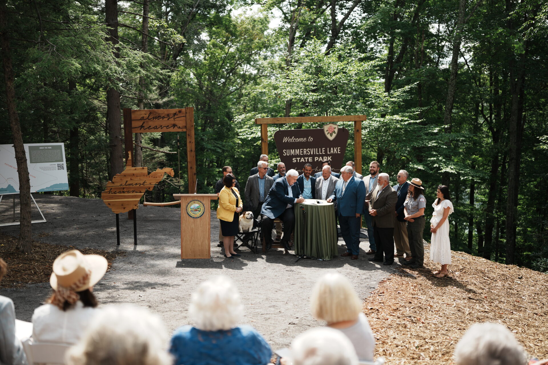 In a forest, a group of people stand and pose as Governor Jim Justice signs a bill into law.