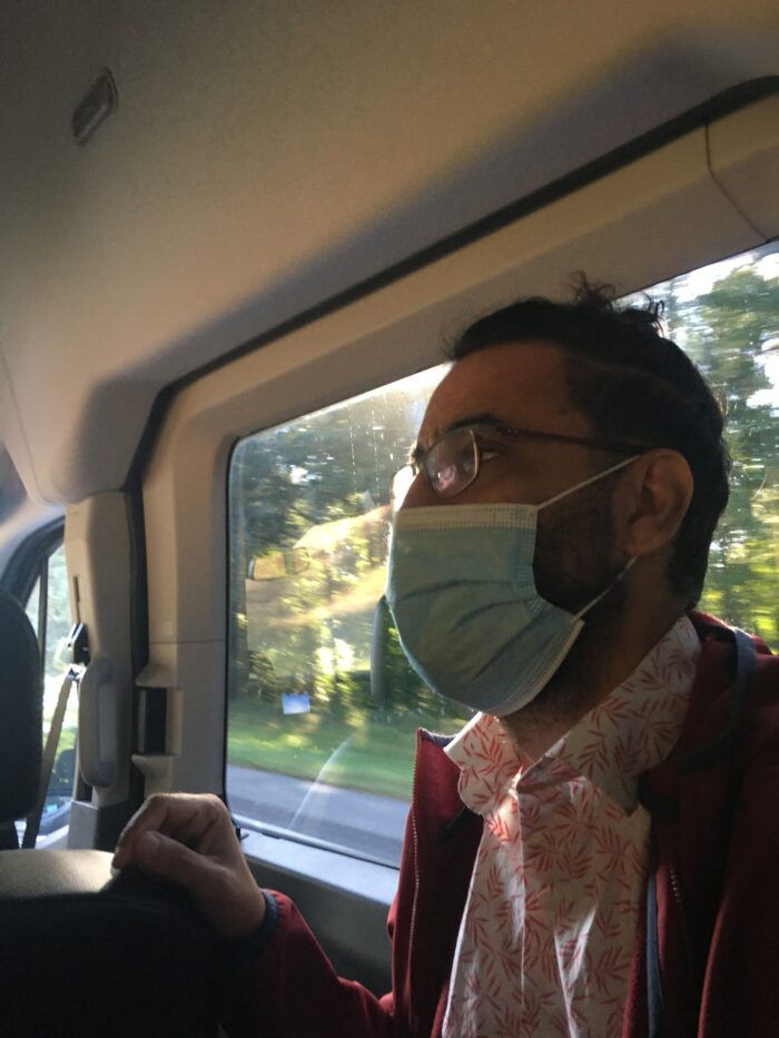 A close up of a man wearing a face mask and glasses on a bus. 