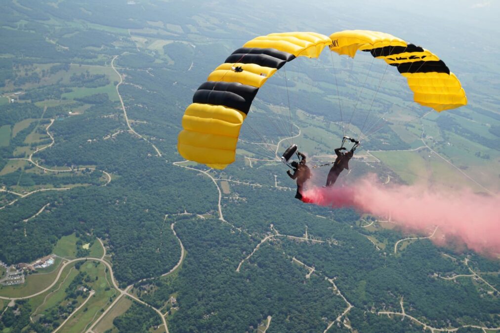 Two people attached to yellow parachutes float through the air.