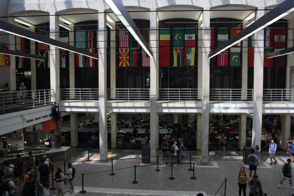 International flags hang behind arches and above an alcove in West Virginia University's student union The Mountainlair. Students can be seen sitting and standing in the hall below.